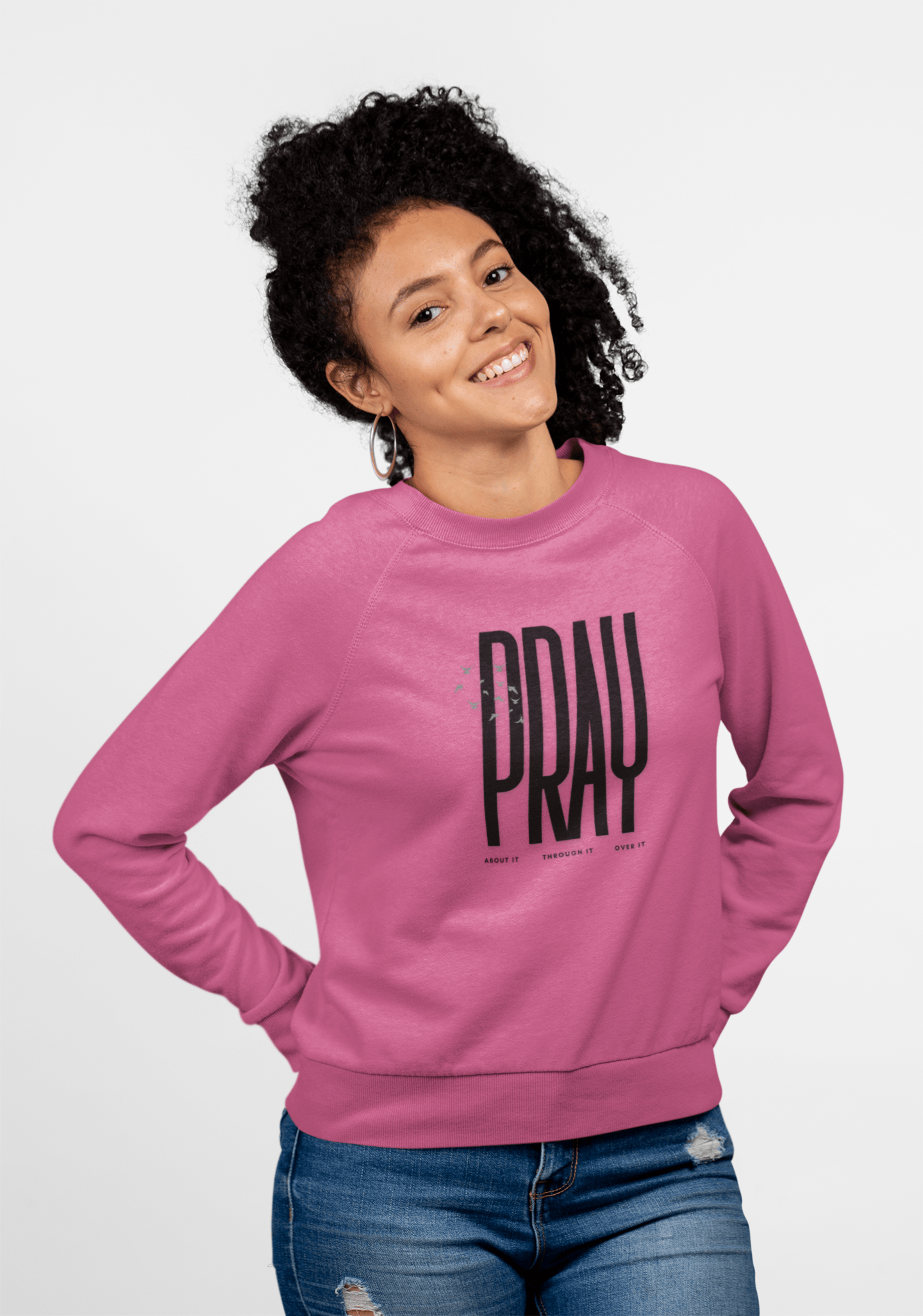 Woman wearing a Heliconia sweatshirt with 'PRAY' printed on it against a white background. Product of Konsecrate